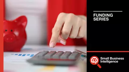 small red piggy bank on the left, hand pressing keys on a calculator figuring out SBA loans for business