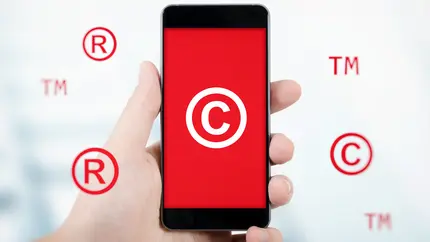 Mobile device in hand displaying red background with trademark and copyright symbols behind the device.