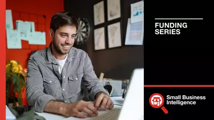 Smiling male entrepreneur sitting at desk viewing funding info for his small business