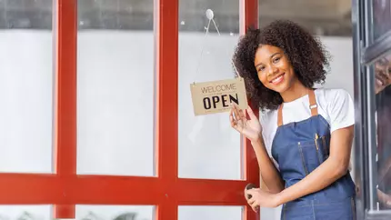 Happy Black female entrepreneur owner standing in front of her small business