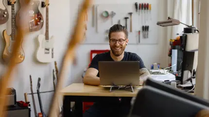 Business owner sitting at desk in studio surrounded by tools and guitars, choosing the right professional liability insurance for his business