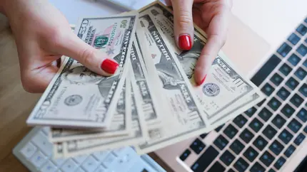 hands with red nail polish fan out money over a computer keyboard. Business owner paying themself