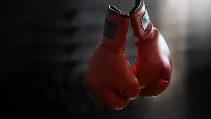 Red boxing gloves dangling over ring. A tribute to the legacy left behind by George Foreman