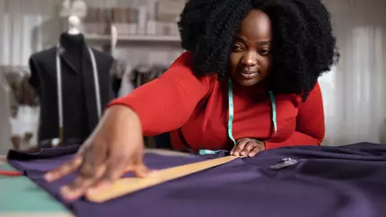 Black woman in red blouse measuring fabric at her small business