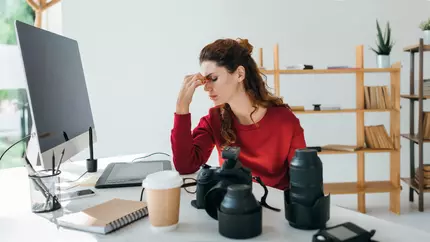 stressed female photographer sitting at desk with tension building trying to handle multiple projects.