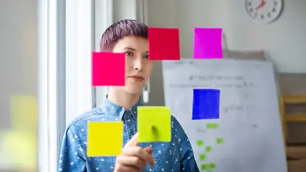 Person organizing brightly colored sticky notes on a glass board while planning business goals and priorities for the new year.