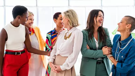 Six women from all backgrounds and race happily sharing their small business stories while casually standing around.