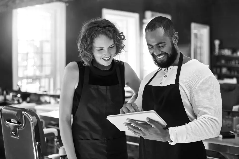Two hairdressers stand together looking at a tablet inside a hair salon