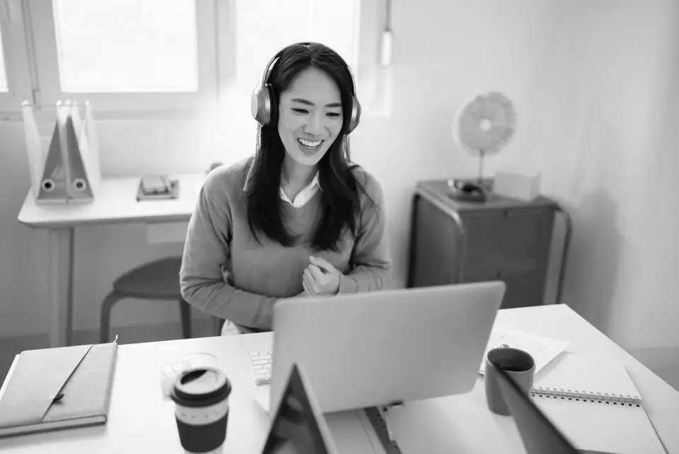 Tutor with headphones on smiling and talking at desk with computer. 