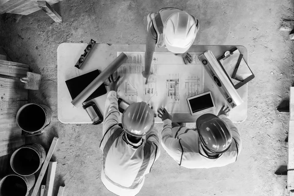 Overhead view of three contractors studying plans over a work bench