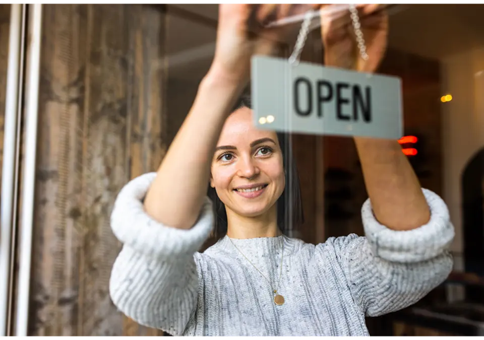 Smiling woman hangs “Open” sign on shop door