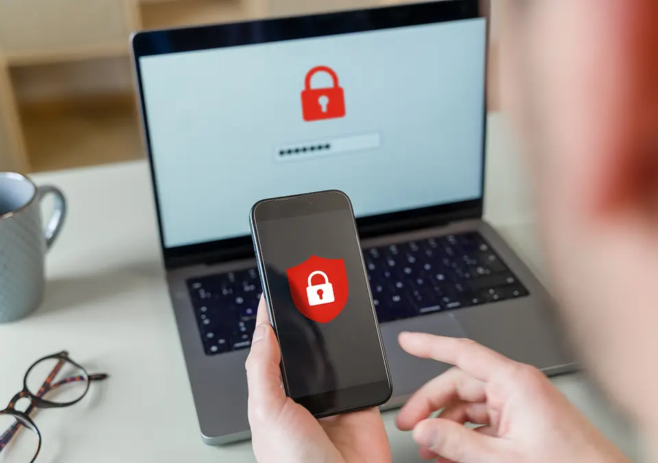 Person holding smartphone with security lock and laptop