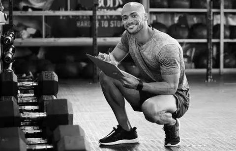 Personal trainer crouching in front of weights with a clipboard, pen and paper 
