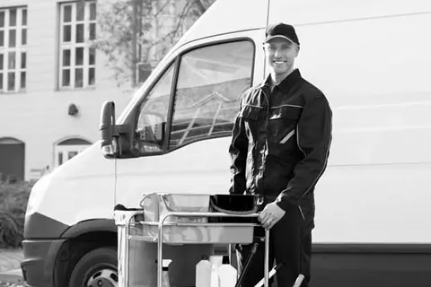 Janitor standing next to a work van with their cleaning supplies