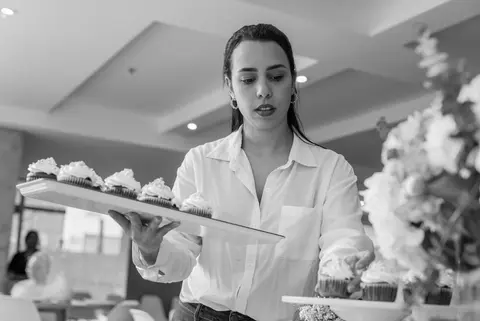 A woman arranges cupcakes on a tray for an event