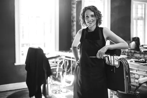 A woman holds scissors and rests arm on a hair salon chair