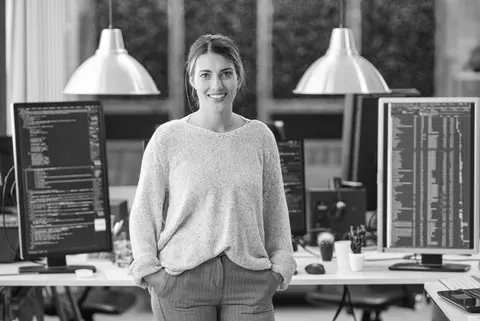 IT Consultant standing and smiling in front of desk with multiple computer screens