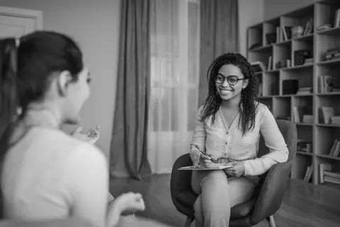 A mental health counselor sits in a chair and listens to a patient during a therapy session