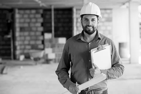A contractor wears a hard hat and holds a clipboard at a job site
