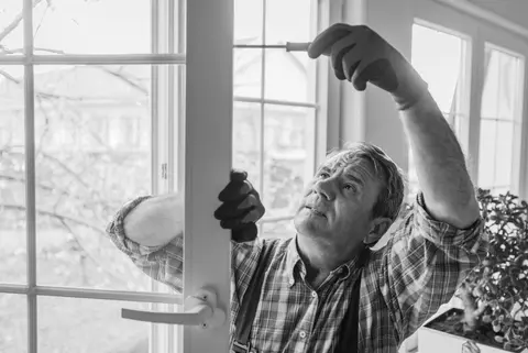 A handyman fixes a window-paned door with a screwdriver