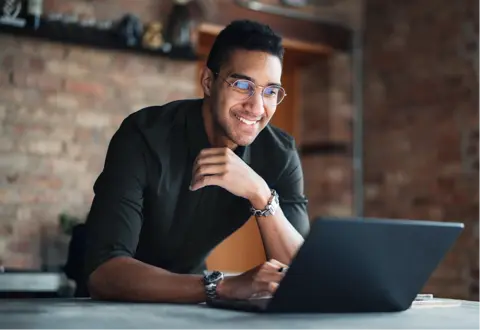Man smiles while typing on a laptop on a desk
