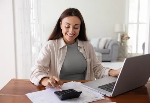 Woman typing on a calculator and laptop on a wooden table