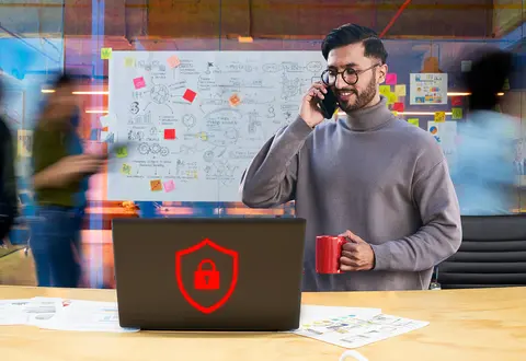 Businessman on phone beside laptop with security shield icon